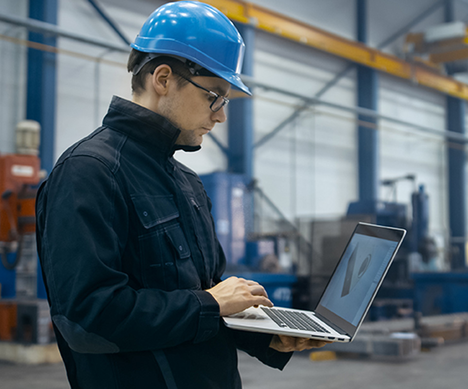 Employee in a facility typing on a laptop, symbolizing the role of IT internal auditors in ensuring system compliance.